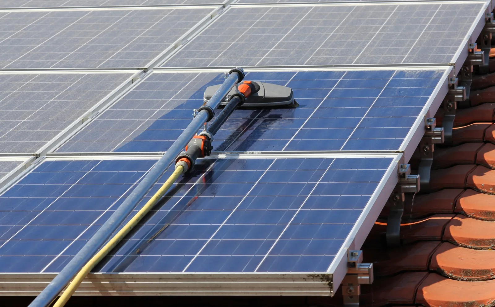 Solar panel cleaning brush and water-fed pole in use on a roof-mounted array